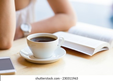 Woman Reading Book And Drinking Coffee At Cafe