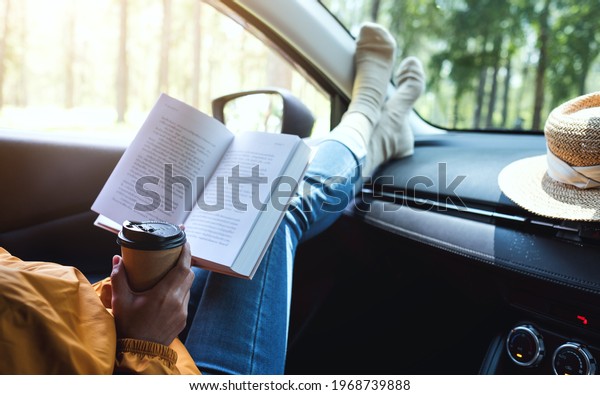 A woman\
reading book and drinking coffee in the\
car