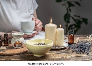 Woman is reading a book and drinking tea in atmosphere of harmony and relaxation. Aroma lamp with essential oils and burning candles on the wooden table. - Shutterstock ID 2129469197