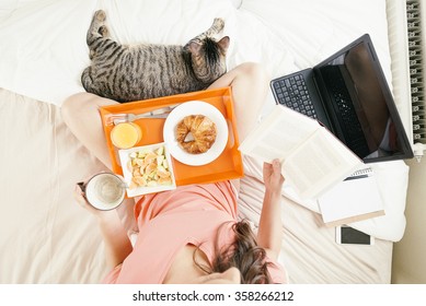 Woman Reading The Book And Having Breakfast. She Is In Her Bedroom. Overhead View