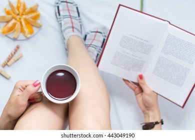 Woman reading a book and having cup of tea in bed