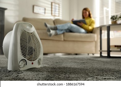Woman reading book in living room, focus on electric fan heater