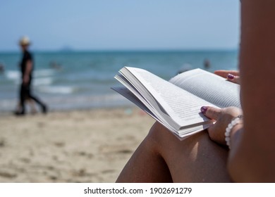 Woman Reading A Book On The Beach, Blurred Background. Summer Leisure On The Beach.