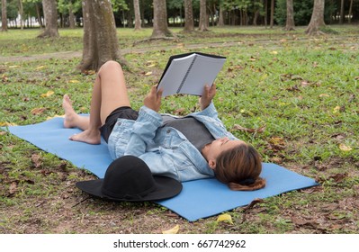 Woman reading a book on a lawn in a park.