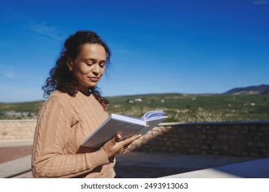 Woman reading book outdoors with scenic landscape background under clear blue sky - Powered by Shutterstock