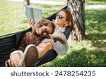 Woman reading book relaxing in hammock with her fluffy brown Maltipoo dog on sunny day. Both looking content and happy. This outdoor scene captures joy of bonding with pets and enjoying togetherness