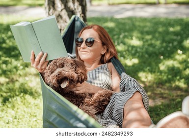 Woman reading book relaxing in hammock with her fluffy brown Maltipoo dog on sunny day. Both looking content and happy. This outdoor scene captures joy of bonding with pets and enjoying togetherness - Powered by Shutterstock