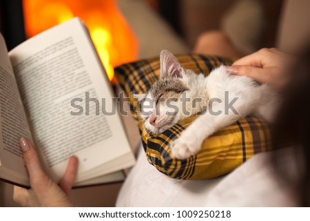 Woman reading by the fire and comforting her rescue kitten - purrfect evening relaxation, closeup, shallow depth