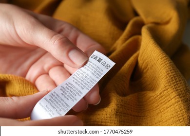 Woman Reading Clothing Label With Care Instructions On Yellow Garment, Closeup