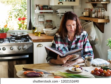 Woman Reading A Cookbook In The Kitchen