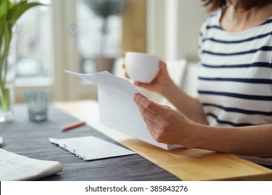 Woman reading a document at the dining table as she enjoys a morning cup of coffee, close up view of her hands - Shutterstock ID 385843276