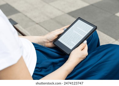 woman reading an e-book sitting on a park bench. reading a book outdoors. High quality photo - Powered by Shutterstock