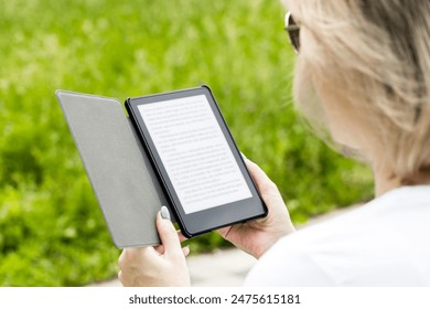 woman reading an e-book sitting on a park bench. man reading an e-book in the park. reading a book outdoors. reading an e-book.  - Powered by Shutterstock