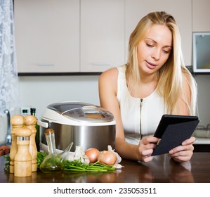 Woman  Reading Ereader And Cooking With New Crockpot At Home Interior