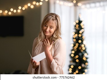 Woman Reading A Heartfelt Message, Note, Book Or Card.   She Is Smiling And Has Her Hand To Heart.