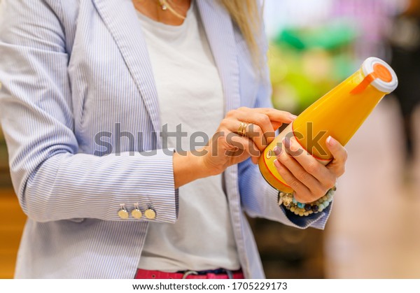 Woman reading ingredients and nutrition\
information on juice bottle\'s etiquette\

