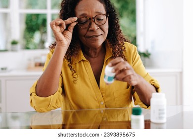 Woman reading the label on her prescription medication as she adheres to her treatment routine at home. Senior woman taking proactive steps to manage her chronic disease and maintain her health. - Powered by Shutterstock