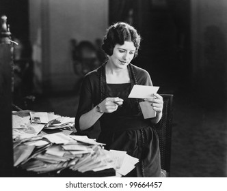 Woman Reading Letter With Pile Of Mail