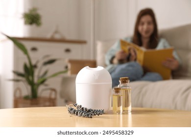 Woman reading magazine at home, focus on aroma diffuser, bottles of essential oils and lavender flowers - Powered by Shutterstock