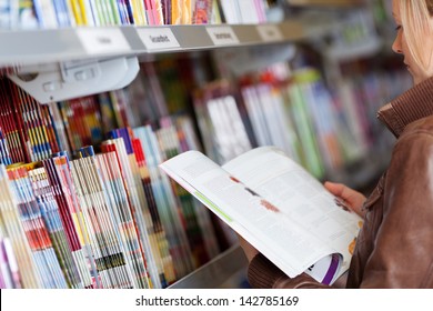 Woman Reading A Magazine Which She Has Just Removed For A Display On A Shelf In A Supermarket