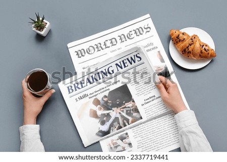 Woman reading newspaper with coffee and croissant on grey background