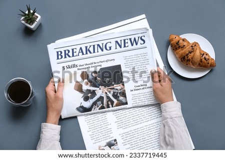 Woman reading newspaper with coffee and croissant on grey background