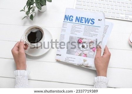 Woman reading newspaper at workplace with cup of coffee on white wooden background