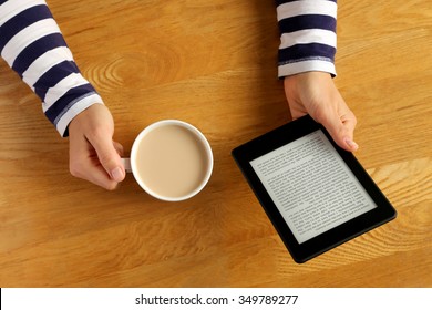 Woman reading a novel on a tablet and drinking her coffee. 