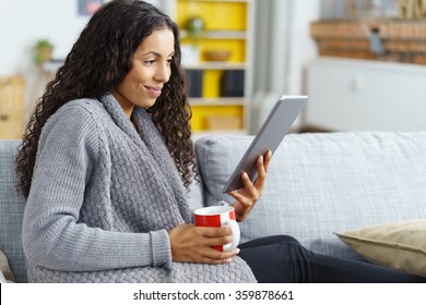 Woman Reading On Tablet At Home With A Cup Of Coffee In Her Hand