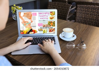 Woman Reading Online Magazine On Laptop In Cafe, Closeup
