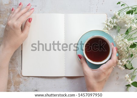 Woman is reading an open blank page book with a copy space and drinking a tea from a cup on a old white wooden table background.