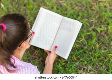 Woman reading an open book on the grass background.