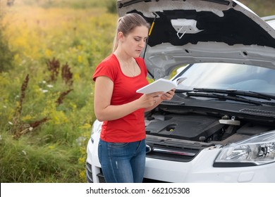 Woman Reading Owner Manual At Broken Car In Meadow