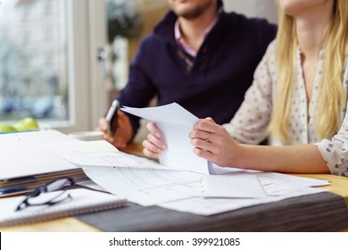 Woman reading a paper document as she sits at a table at home with her husband balancing the books , close up view of her hands and the paperwork