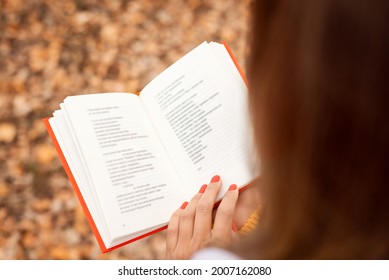 Woman reading poems in autumn park. Back view of opened book with red cover in hands of a girl. - Shutterstock ID 2007162080