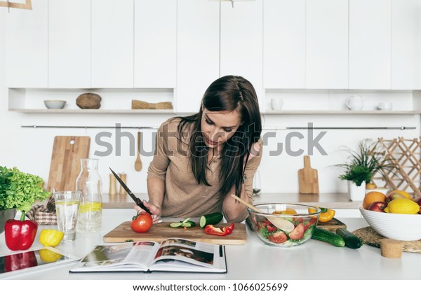 Woman reading recipe for simple summer salad\
in cookbook. Simple healthy food\
concept