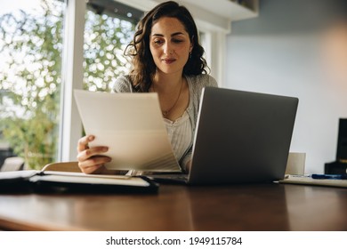 Woman reading some document while working on laptop. Female working from home. - Powered by Shutterstock