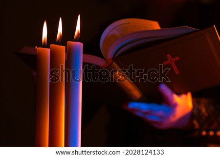 Woman reads Bible by the light of three candles. Christianity concept. Protestantism, Catholicism and Orthodoxy. Catholic woman communicates with God. Reading religious literature. Faith in God.