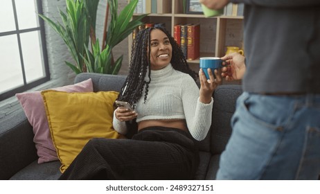 Woman receives coffee from man while using smartphone, cozy interaction in modern living room setting - Powered by Shutterstock