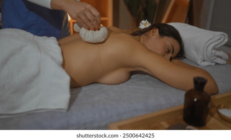 A woman receives a relaxing massage therapy at a wellness spa, with another woman applying a herbal compress on her back. - Powered by Shutterstock