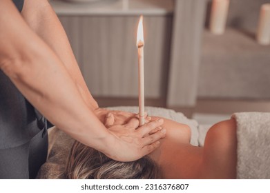 A woman receiving an ear candle treatment from a masseur. - Powered by Shutterstock