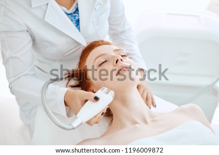 Woman receiving electric facial ultrusound peeling at modern beauty salon. Female patient getting radio frequency lifting on her face.