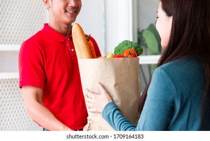 Woman receiving fresh food in paper bag or paper container from delivery man at the door. Postman delivery packet of food, vegetable to recipient at home. Food delivery, shopping online and transport - Shutterstock ID 1709164183
