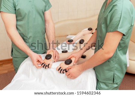 Woman receiving hot stone massage on feet and toes by two massage therapists.