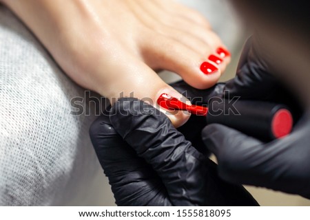Woman receiving nail polishing with red nail polish on fingers of feet by professional podiatrist close up.