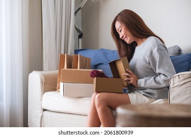 A Woman Receiving And Opening A Postal Parcel Box Of Clothing At Home For Delivery And Online Shopping Concept