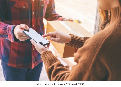 Woman Receiving Parcel Box And Signing Name On The Phone From Delivery Man At The House's Door