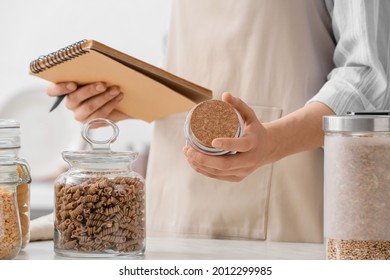 Woman With Recipe Book And Different Products In Kitchen