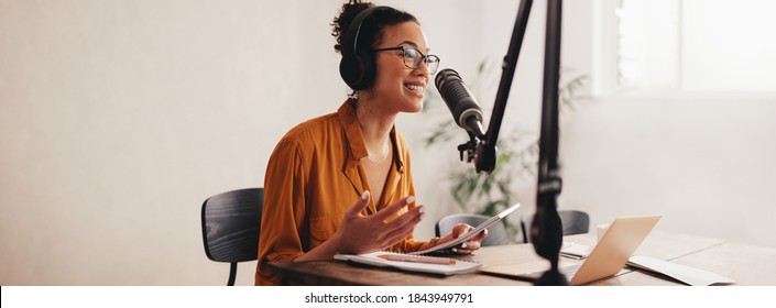 Mulher gravando um podcast em seu laptop com fones de ouvido e um microscópio. Podcaster feminina fazendo podcast de áudio de seu estúdio em casa.