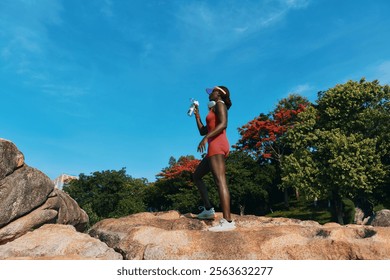 Woman in red activewear enjoying outdoor exercise on a rock under a clear blue sky - Powered by Shutterstock